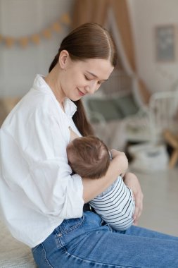 Mutlu gülümseyen genç anne yeni doğmuş bebekle yatak odasında oynuyor. Ebeveynlik kavramı