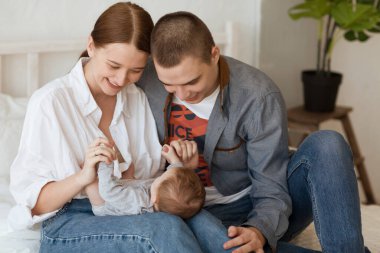 Gülümseyen genç anne ve baba yeni doğan kızlarını evde bir yatakta tutuyorlar.