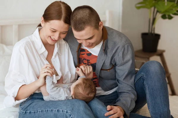 Gülümseyen genç anne ve baba yeni doğan kızlarını evde bir yatakta tutuyorlar.
