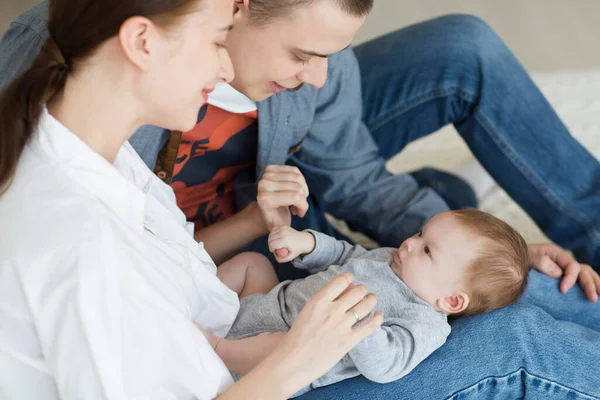 Gülümseyen genç anne ve baba yeni doğan kızlarını evde bir yatakta tutuyorlar.