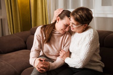 Yaşlı anne teselli ediyor, evde kanepede oturan üzgün yetişkin kızı teselli ediyor. iki nesil boyunca destek
