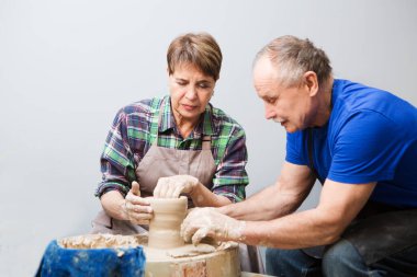 Çömlekçide çömlek boyama atölyesinde günlük giysiler ve önlükler içinde kıdemli bir çift. Emekli maaşıyla hobi