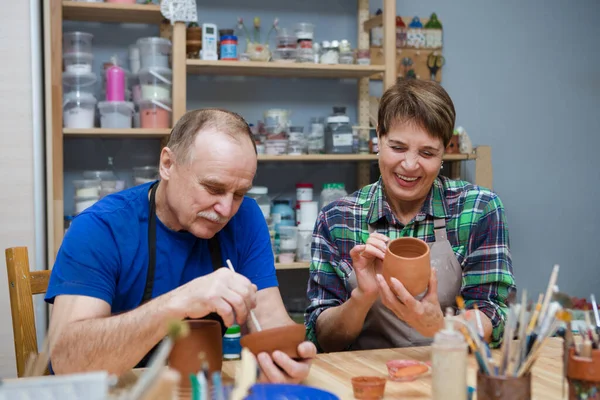Çömlekçide çömlek boyama atölyesinde günlük giysiler ve önlükler içinde kıdemli bir çift. Emekli maaşıyla hobi