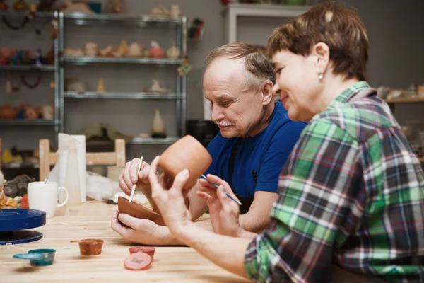Çömlekçide çömlek boyama atölyesinde günlük giysiler ve önlükler içinde kıdemli bir çift. Emekli maaşıyla hobi