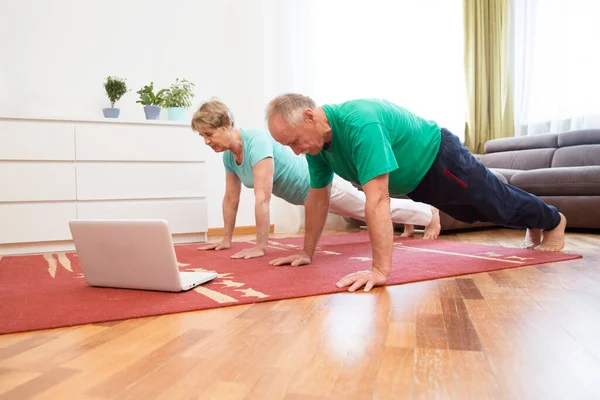 active senior couple doing stretching exercise and watching online workout tutorials on the laptop in living room at home. home fitness, activewear.