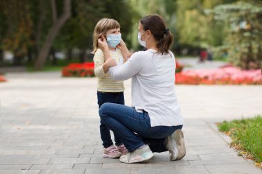 Tıbbi maske takan bir anne, kızına açık havada bir güvenlik maskesi takıyor. yeni normal.