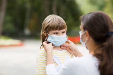 Tıbbi maske takan bir anne, kızına açık havada bir güvenlik maskesi takıyor. yeni normal.