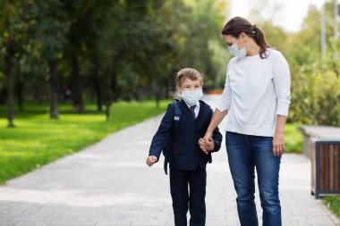 Anne ve okul çocuğu maskeli ve sırt çantalı okula gidiyorlar. kopyalama alanı. yeni normal