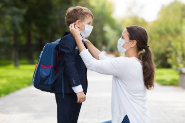 Anne ve okul çocuğu maskeli ve sırt çantalı okula gidiyorlar. kopyalama alanı. yeni normal
