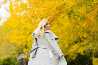 Güzel sarışın kadın sonbahar parkında eğleniyor.