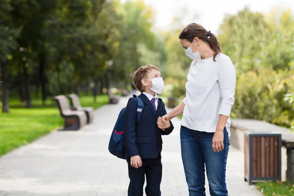 mom and her son schoolboy wearing mask with backpack going to school. copy space. new normal