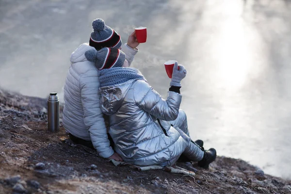 Couple drinking hot coffee or tea and sitting next to a stunning winter landscape. Concept of travel and adventure. Zero waste travel