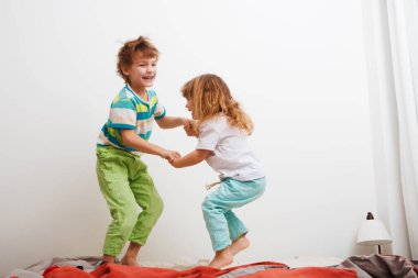 Çocuklar erkek kardeş ve kız kardeş oynuyorlar ve yatakta zıplıyorlar. aile sabahı.