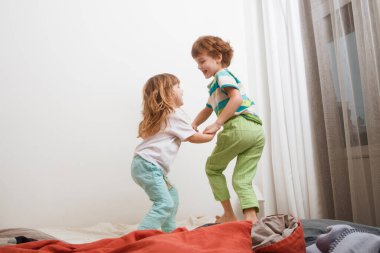 Çocuklar erkek kardeş ve kız kardeş oynuyorlar ve yatakta zıplıyorlar. aile sabahı.