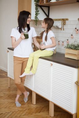 Gülümseyen anne ve kızı mutfaktaki kavanozda samanla birlikte sağlıklı yeşil meyve suyu içerler. Sağlıklı Yaşam Tarzı.