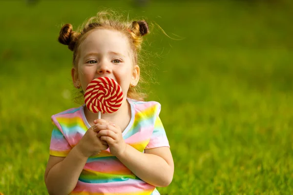 Little girl with red lollipop in summer in the park.