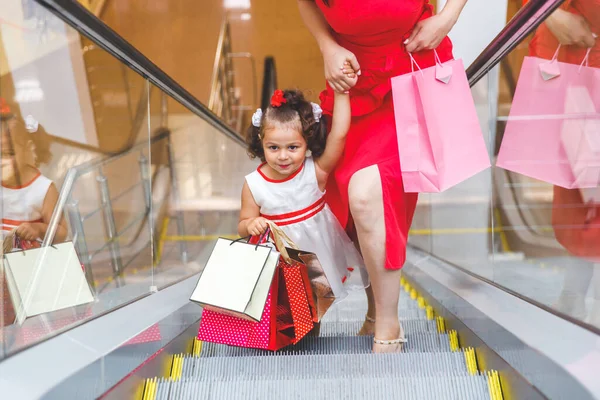 mom and daughter on the escalator in the mall with  bags