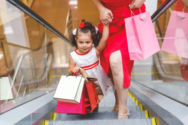 mom and daughter on the escalator in the mall with  bags