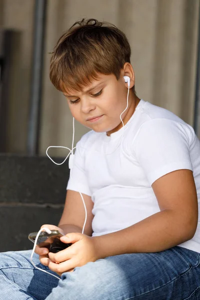 boy in headphones with smartphone listens to music in summer park