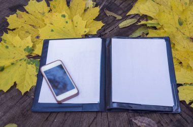 Bir siyah klasör ve cep telefonu sarı yapraklar bir ahşap zemin üzerine beyaz kağıda