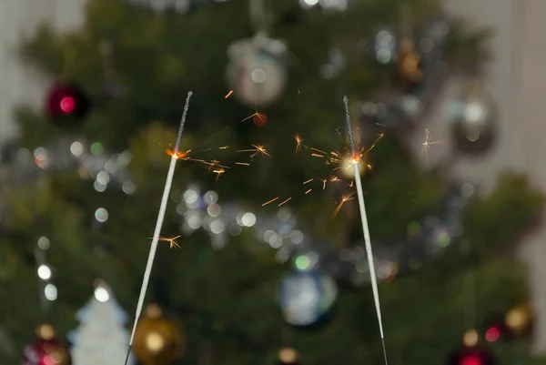 Bengal lights with flying sparks on the background of a Christmas tree, close-up