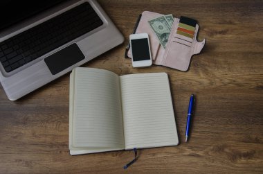 defter bir kalem, bir çanta para ve indirim kartları ile bir dizüstü bilgisayar ve bir ahşap zemin üzerinde bir telefon ile