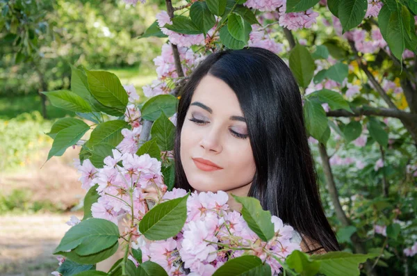ピンクの花に囲まれて 暖かい春の日長い黒髪の美しい少女 — ストック写真