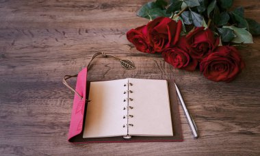 defter bir kalem ve bir ahşap zemin üzerine kırmızı mis kokulu gül buketi ile yazmak için