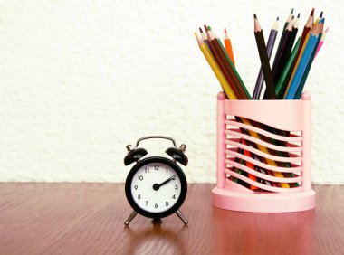 ahşap bir masa üzerinde oklar ve renkli kalemler ile siyah çalar saat