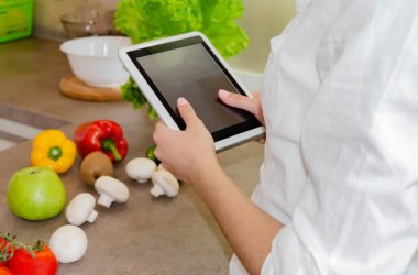 Mutfaktaki sebze ve meyvelerin arka planında kadın ellerinde tablet, yakın plan.