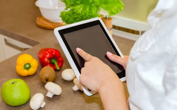 tablet in female hands, on the background of vegetables and fruits in the kitchen, close-up