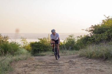 Bisiklet yarışçısı yolculuk yalnız rocky road, göl ve orman arka plan güzel gün batımı sırasında