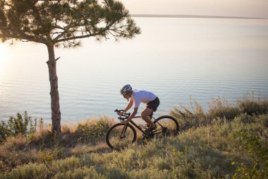 Bisiklet yarışçısı yolculuk yalnız rocky road, göl ve orman arka plan güzel gün batımı sırasında