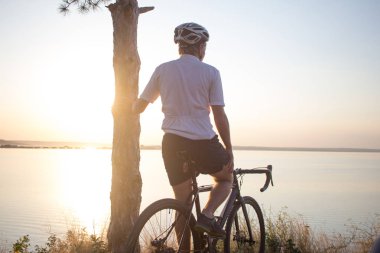 Bisiklet yarışçısı yolculuk yalnız rocky road, göl ve orman arka plan güzel gün batımı sırasında
