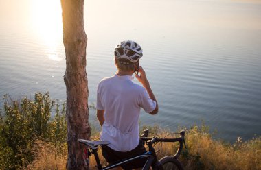 Bisiklet yarışçısı yolculuk yalnız rocky road, göl ve orman arka plan güzel gün batımı sırasında