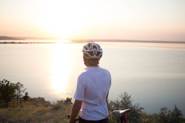 Bisiklet yarışçısı yolculuk yalnız rocky road, göl ve orman arka plan güzel gün batımı sırasında