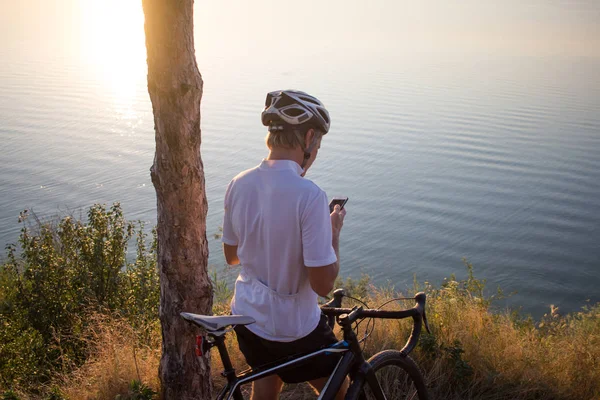 Bisiklet yarışçısı yolculuk yalnız rocky road, göl ve orman arka plan güzel gün batımı sırasında
