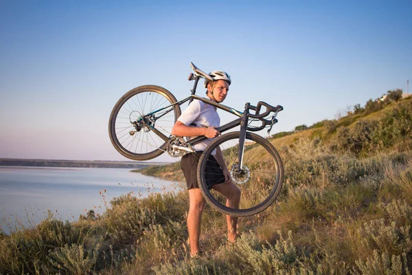 Bisiklet yarışçısı yolculuk yalnız rocky road, göl ve orman arka plan güzel gün batımı sırasında