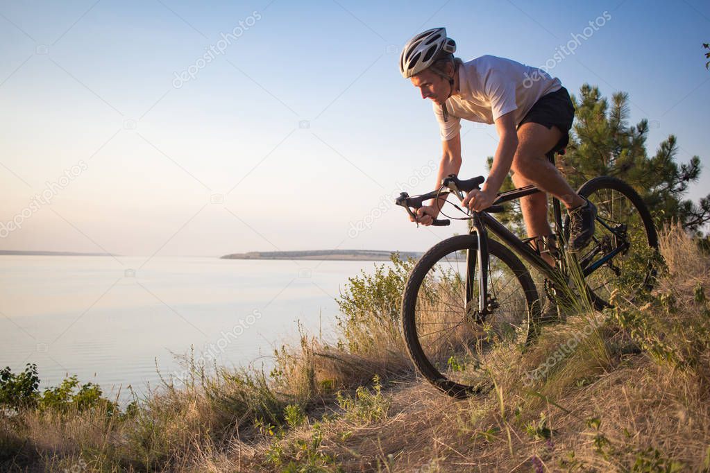 Bicycle racer ride alone on the rocky road, lake and forest background during the beautiful sunset