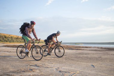 İki genç erkek sırt çantaları ve kask ile bir turne bisikletle binmek açık havada köy yolunda bir bisiklet gezisi