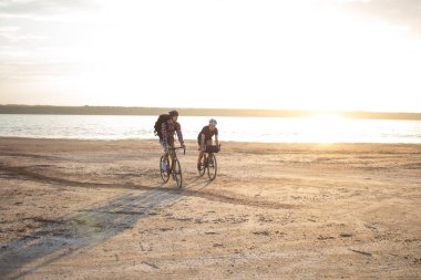 İki genç erkek sırt çantaları ve kask ile bir turne bisikletle binmek açık havada köy yolunda bir bisiklet gezisi