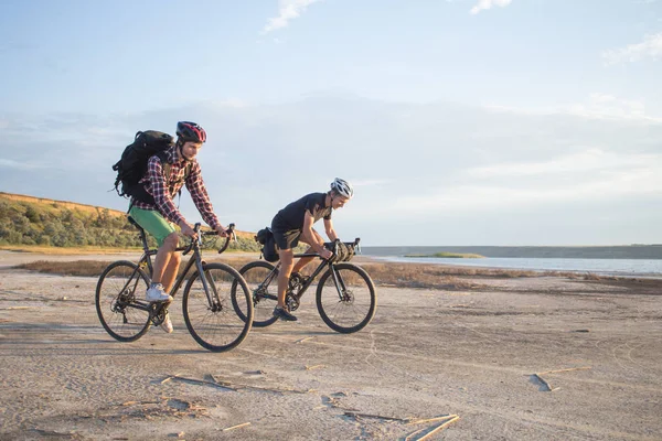İki genç erkek sırt çantaları ve kask ile bir turne bisikletle binmek açık havada köy yolunda bir bisiklet gezisi
