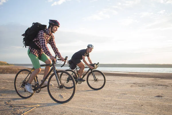 Two young male on a touring bicycle with backpacks and helmets ride outdoors on country road on a bicycle trip