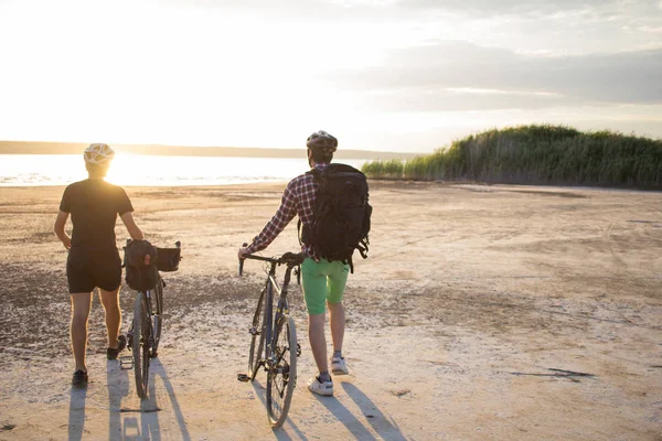 İki genç erkek sırt çantaları ve kask ile bir turne bisikletle binmek açık havada köy yolunda bir bisiklet gezisi