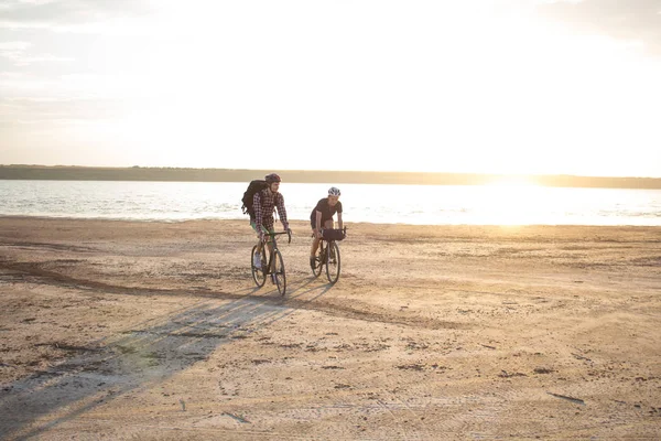 İki genç erkek sırt çantaları ve kask ile bir turne bisikletle binmek açık havada köy yolunda bir bisiklet gezisi