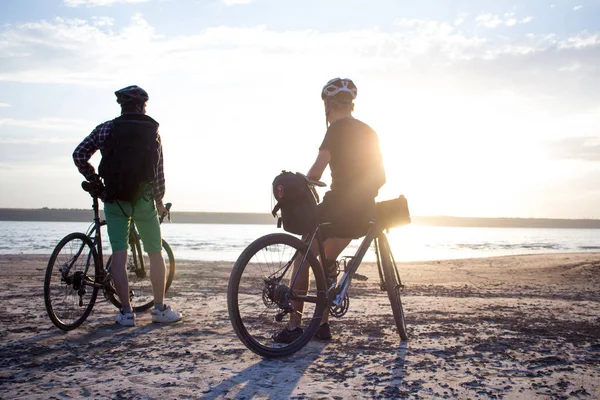 İki genç erkek sırt çantaları ve kask ile bir turne bisikletle binmek açık havada köy yolunda bir bisiklet gezisi