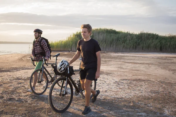 Two young male on a touring bicycle with backpacks and helmets ride outdoors on country road on a bicycle trip