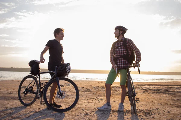 Two young male on a touring bicycle with backpacks and helmets ride outdoors on country road on a bicycle trip