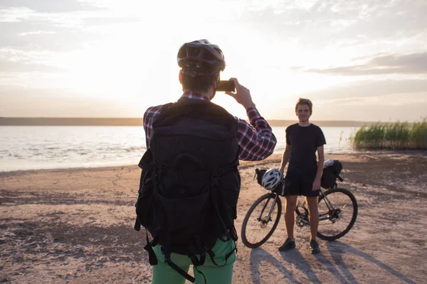 İki genç erkek sırt çantaları ve kask ile bir turne bisikletle binmek açık havada köy yolunda bir bisiklet gezisi