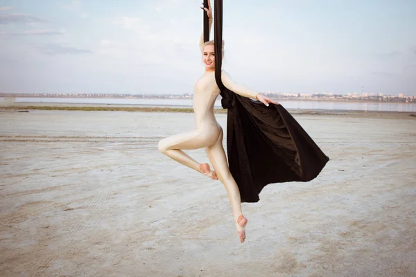 适合妇女在瘦瘦的衣服跳舞与空中丝绸在天空背景下 体操运动员的空中丝绸训练 — 图库照片